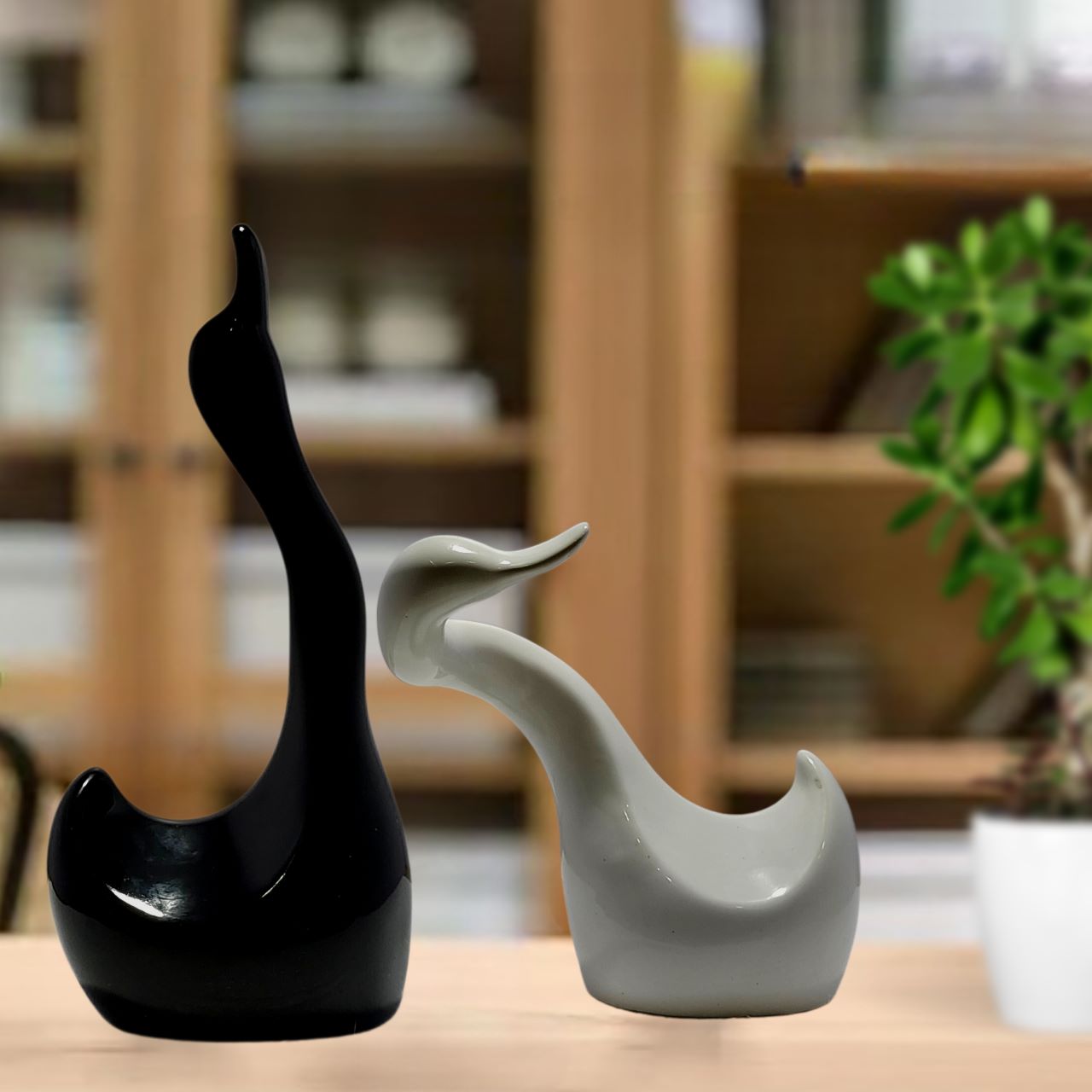 Black and white ceramic duck statues positioned affectionately, with the taller black duck's neck wrapped around the shorter white duck on a kitchen counter.