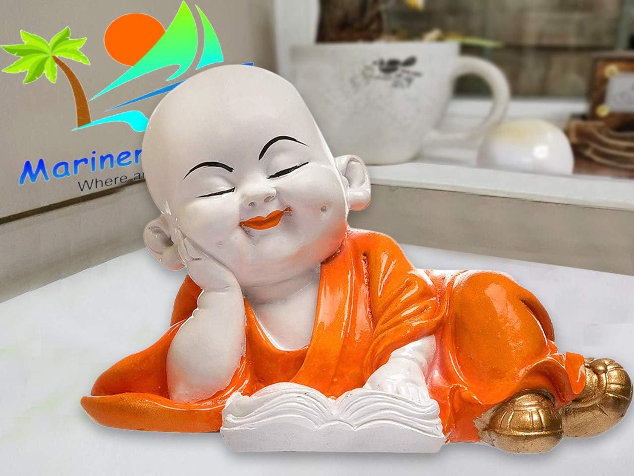 Orange Laughing Buddha Statue reading a book, positioned on a kitchen counter, adding a vibrant touch of happiness to the space.